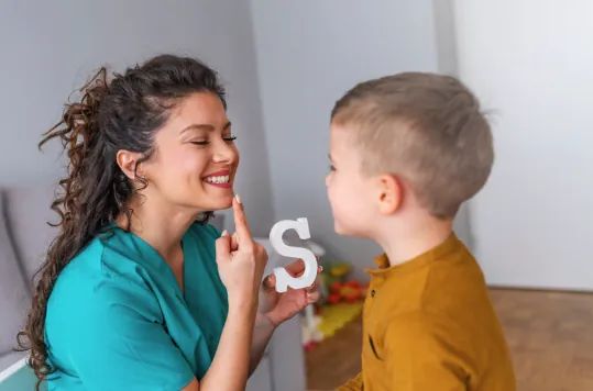 A speech pathologist helping a young boy practise the letter S sound